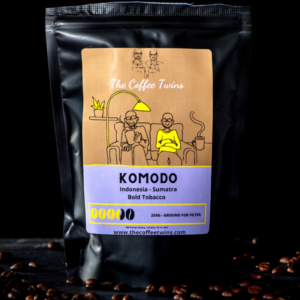 Black coffee bag labeled 'Komodo' with illustrations of two characters and coffee details.