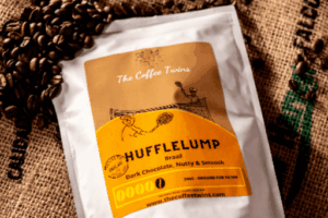 Bag of Hufflelump Swiss Water Decaf coffee beans from The Coffee Twins standing beside a freshly brewed cup of coffee. Brazilian speciality coffee with 99.9% of caffeine removed using the Swiss Water decaffeination process.