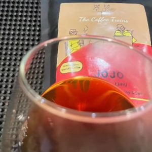A glass of coffee in front of a coffee bag from The Coffee Twins labeled 'JOJO Limu'.