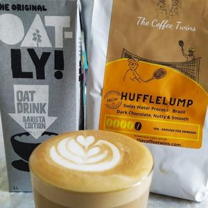 Oatly Barista Edition oat drink carton next to Hufflelump coffee bag from The Coffee Twins and a latte with latte art.