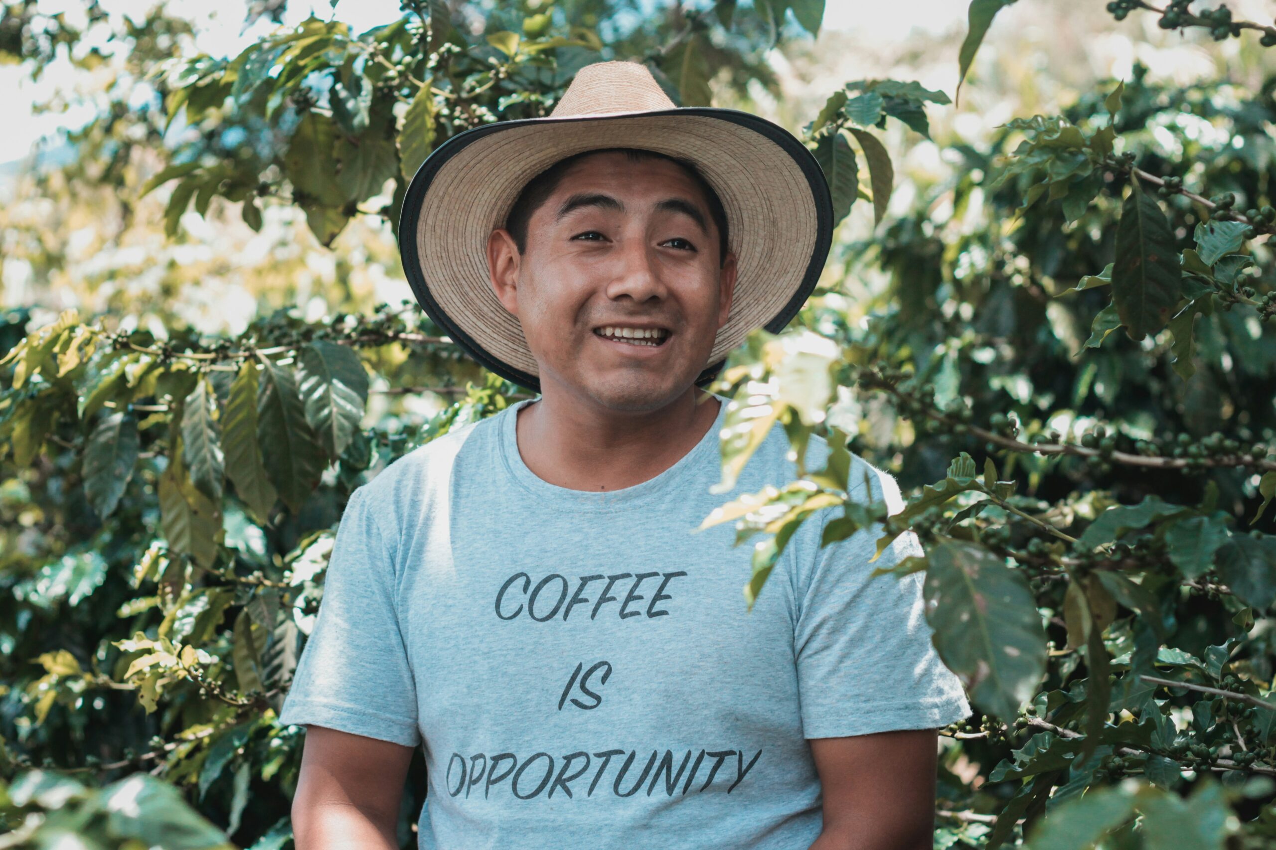 A coffee farmer wearing a straw hat and a t-shirt that says 'COFFEE IS OPPORTUNITY'.