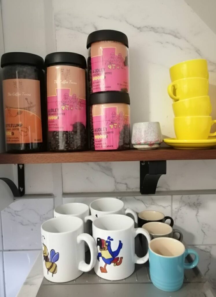 Containers of coffee and various mugs displayed on a shelf from The Coffee Twins.