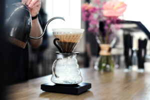 A person pouring hot water from a kettle into a V60 coffee dripper placed on a glass carafe.