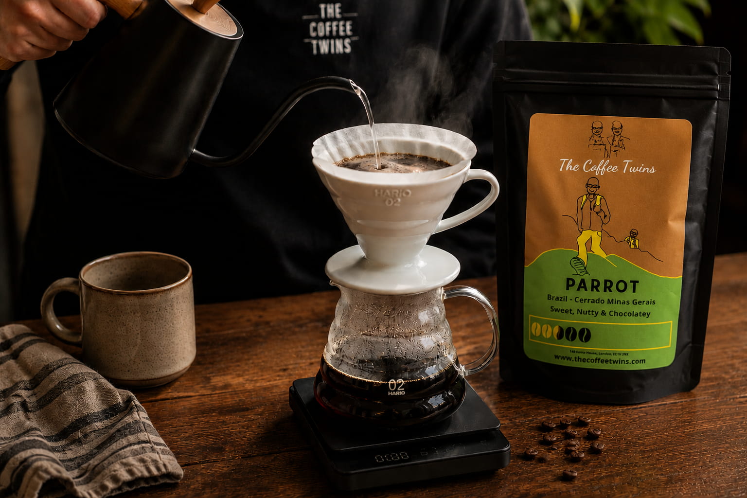 Hand pouring hot water over a Hario V60 pour-over coffee dripper beside The Coffee Twins Parrot speciality coffee beans, demonstrating the V60 coffee brewing method at home.