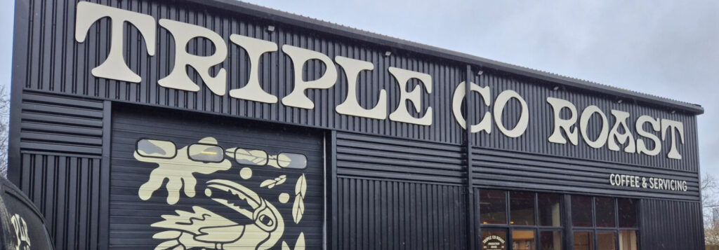 Triple Co Roast coffee roastery building with large exterior signage, featuring its distinctive bird mural and Coffee & Servicing entrance.